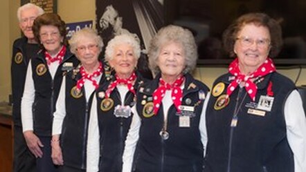 Five people wearing vests with the National Park Service symbol and red and white polka dotted scarves face the camera smiling