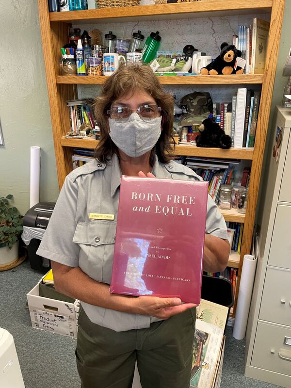 Superintendent Johnson holds a copy of the new edition of Born Free and Equal in front of a bookcase full of National Park paraphenalia