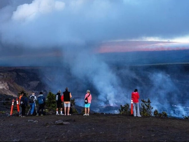 A group of people stands along the rim of a crater with a great deal of steam coming up