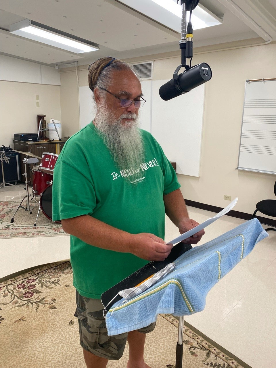 A voice actor stands at a podium reading from a script into a manuscript