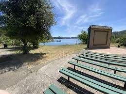 Several rows of green benches face a dais, a lake, and trees